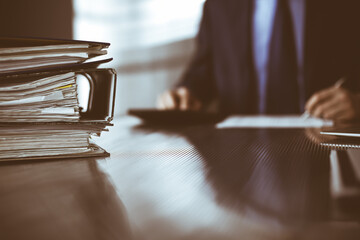 Binders with papers are waiting to be processed by man accountant in blue blazer staying at home during covid pandemic. Taxes and audit concept. Internal Revenue Service inspector checking financial