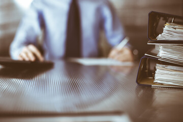 Binders with papers are waiting to be processed by man accountant in blue shirt staying at home during covid pandemic. Taxes and audit concept