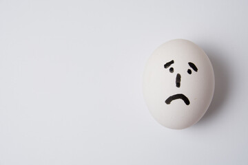 Egg with a sad and frustrated face, on a white background copy space.