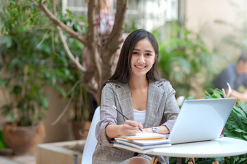 Fototapeta premium Beautiful Asian woman sitting taking notes at a coffee shop. Looking at camera.