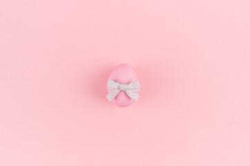 Pink easter egg with grey ribbon standing on pastel pink background, copy space.