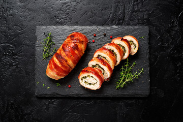 Bacon wrapped chicken rolls stuffed with feta cheese and spinach on black stone background. Beautiful festive lunch or dinner. top view