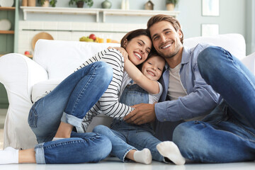 Young Caucasian family with small daughter pose relax on floor in living room, smiling little girl kid hug embrace parents, show love and gratitude, rest at home together. - obrazy, fototapety, plakaty