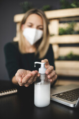 pretty, young blond businesswoman is sitting in a sustainable, ecological office wearing a protective mask and disinfecting her hands because of corona