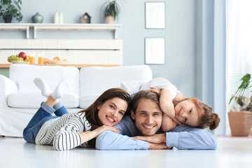 Young Caucasian family with small daughter pose relax on floor in living room, smiling little girl...