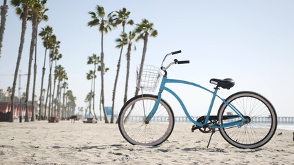 Blue bicycle, cruiser bike by sandy ocean beach, pacific coast near Oceanside pier, California USA. Summertime vacations, sea shore. Vintage cycle, tropical palm trees, lifeguard tower watchtower hut - obrazy, fototapety, plakaty