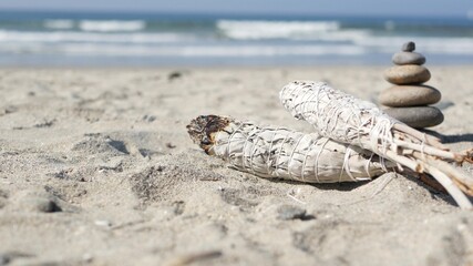 Dried white sage smoke, smudge stick burning in soft focus with bokeh, aroma smudging close up. Rock balancing on ocean beach, stones stacking by sea water waves. Zen pyramid of pebbles on sandy shore