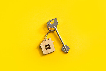 Key chain in the shape of wooden house with key on a yellow background. Building, design, project,...