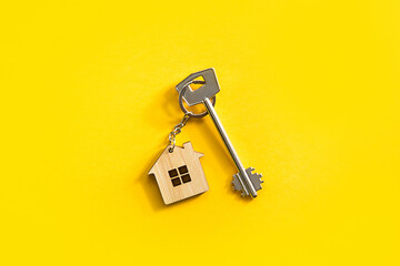 Key chain in the shape of wooden house with key on a yellow background. Building, design, project, moving to new home, mortgage, rent and purchase real estate. Copy space