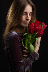 Studio portrait of a young woman on black background with a bouquet of red tulips in her hands