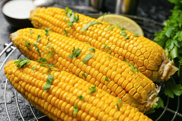 Tasty baked corn cobs on dark background