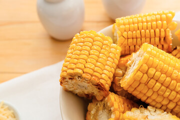 Plate with tasty baked corn cobs on wooden background
