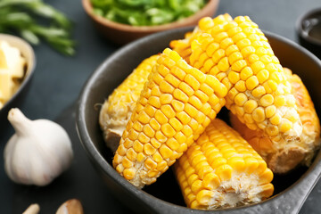 Frying pan with tasty baked corn cobs on dark background