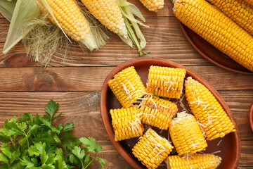 Baking dish with tasty baked corn cobs on wooden background