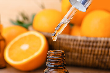 Orange essential oil dripping from pipette into bottle, closeup