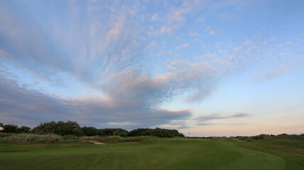 Naklejka na ściany i meble Golfcourse with clouds and sunrise with beautiful green grass and sky