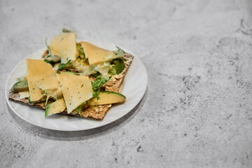 Top view. Sandwich rye diet bread with butter, cheese, avocado and lettuce on a white plate on a gray concrete background. Healthy food for weight loss. Photo for recipes. Shallow depth of field.