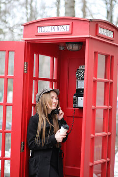 Beautiful young girl in a phone booth. The girl is talking on the phone from the payphone. English telephone booth in the street and a woman talking on phone.
