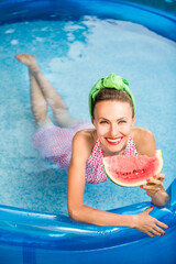 shot of attractive sexy woman in swimming suit posing in pool with watermelon