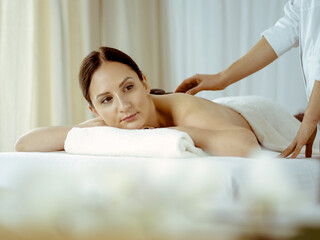 Obraz na płótnie Canvas Pretty brunette woman enjoying treatment with hot stones in spa salon. Beauty concept