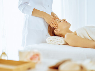Obraz na płótnie Canvas Beautiful woman enjoying facial massage with closed eyes in spa center. Relax treatment concept in medicine