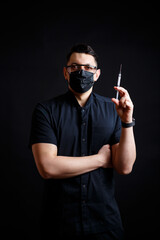 Male doctor chief physician in a black surgical suit. Close-up portrait. Holds a syringe with a vaccine. Covid-19 drug