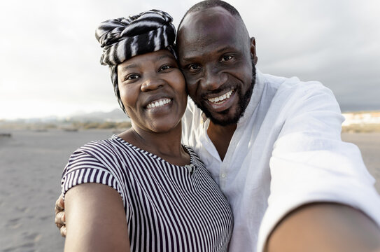 Happy African couple taking selfie on the beach with mobile smartphone camera during summer vacation - Love relationship concept
