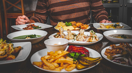 man hands with a knife and fork at a table with many different food