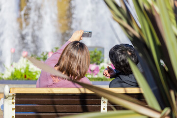 噴水のある公園のベンチで自撮りをする男女