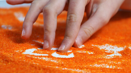 sand therapy, children's hand draws on the orange kinetic sand
