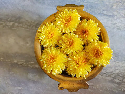 Overhead Shot Of Yellow Flowers In A Wooden Bowl On A Marble Table