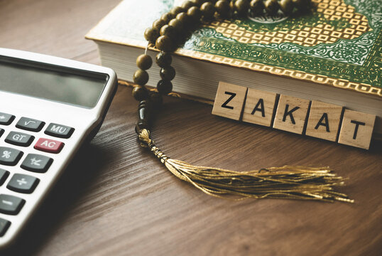 Concept of zakat in Islam religion. Selective focus of wooden alphabet, calculator, rosary beads and Quran on wooden background.