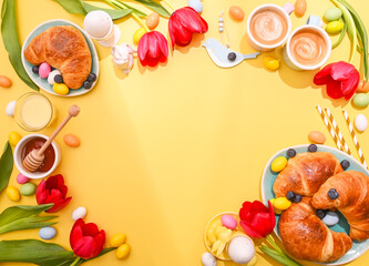Spring Easter breakfast. Two Espresso coffee in bright cups, Easter chocolate eggs, pink bunny ears and red tulips on a yellow background. Above. Copy space. Flat lay