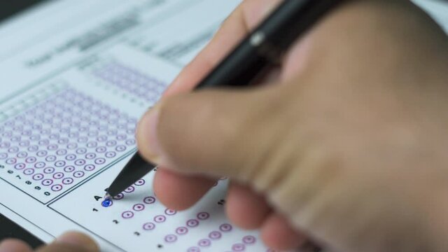Education and exam concept. Answering multiple-choice test questions. A student filling out test sheet. Student hand with pen fill in exam test answer sheet. Answering test questions on the exam