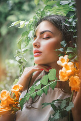 Beautiful young woman posing in Trumpet vine flowers in summer garden. Beauty model girl with Campsis. Enjoying nature outdoor. 