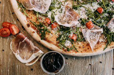 Pizza with bacon arugula and tomatoes. Top down view on delicious single round pizza with arugula lettuce and bacon meat toppings