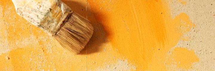 Paintbrush in front of the orange color wall. Panoramic image