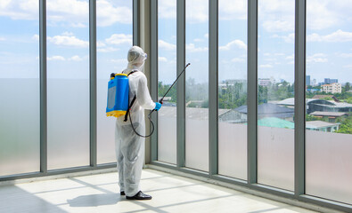 Officer wearing sterilize protective suit with chemical tank on back spraying Disinfectant solution in office place to reduce and protect coronavirus