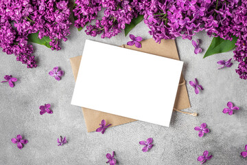 Flower composition. Blank greeting card and envelope with lilac flowers on gray concrete background. top view. flat lay