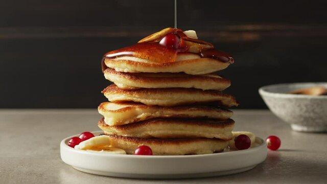 honey or mapple syrup pouring on stack of freshly baked pancakes decorated with banana and berries