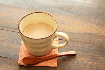 Latte to drink in a handmade cup on a wooden table. Use a wooden spoon. Place the orange coaster under the cup.
