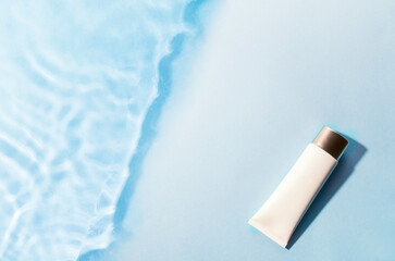 Tube of sunscreen on blue water surface. Cosmetic cream lotion, sunscreen on blue background of...