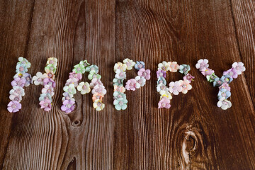 The word HAPPY is lined with letters on a dark wooden background in multicolored flowers.