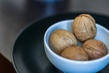 Heap, four whole walnuts in a round-shaped brown shell lie in a small white platter in black plate on table blurred bokeh background. Macro. Close-up
