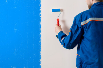 worker painter painting the wall surface with a roller, man at work decorating a room