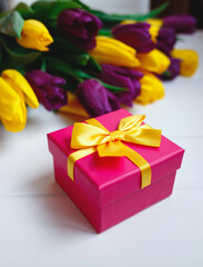 pink gift box with yellow bow on the background of a bouquet of tulips