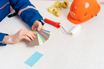 male worker holding roller and color swatch samples to paint the wall in the room