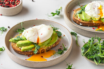 Healthy breakfast. Whole wheat toasted bread with avocado, poached egg, soft cheese and sprouts on white background
