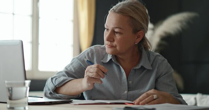 Concentrated 50s woman   listening educational lecture online meeting business video call, writing notes, working at home, remote work 