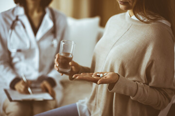 Close-up woman-patient holding pills near her doctor, time to take medications, cure for headache or remedy pain killer drugs. Stay at home concept during Coronavirus pandemic and self isolation